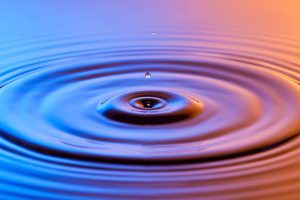 Water Drop Close Up With Concentric Ripples Colourful Blue And Amber Surface